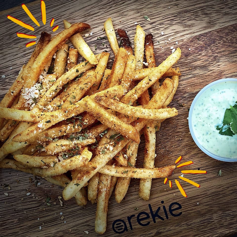 Seasoned golden fries piled on a wooden table beside a bowl of creamy herb dipping sauce.
